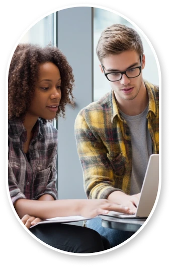 A diverse pair of graduate students reviewing documents together in university building, pointing at laptop screen in discussion