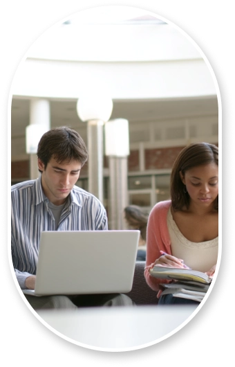Diverse graduate students in casual professional attire studying in bright university commons area, individual focus with laptops and materials